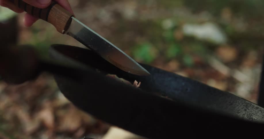 A camper uses a knife to stir the eggs and bacon being cooked in a cast iron pan