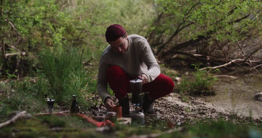 A man pours a cup of coffee hands it to his girlfriend and gives her a kiss as they hug and look at the mountains