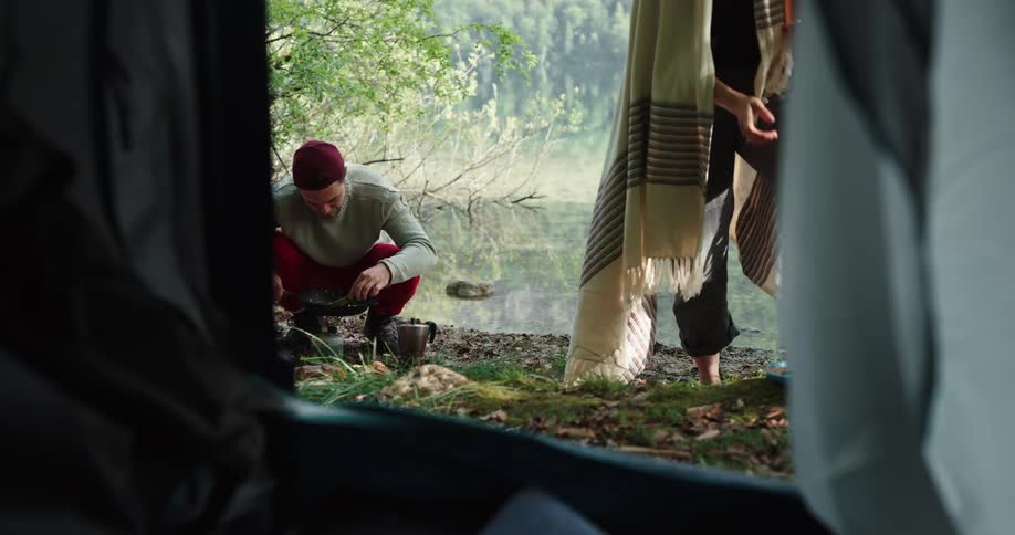 A man and woman are eating a meal outside a tent near water