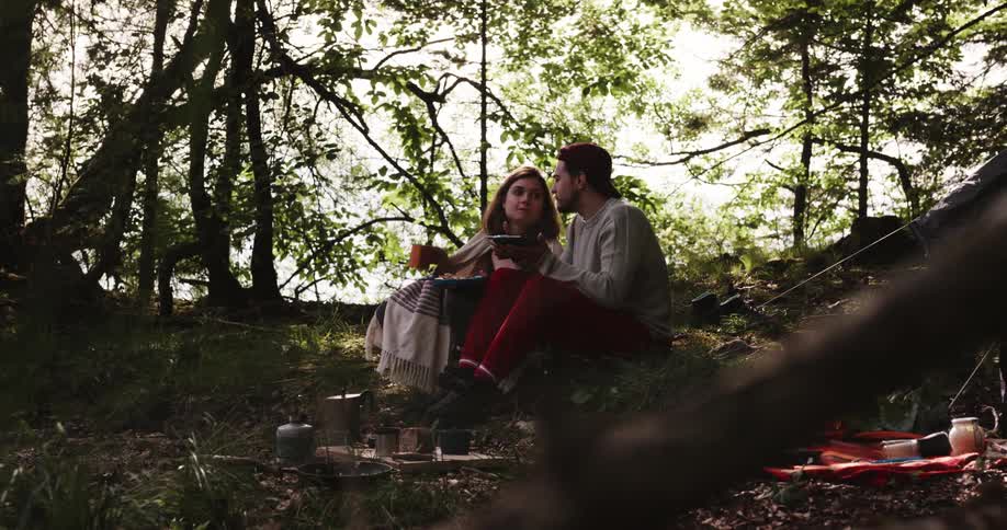 Man and woman eat food in the woods while camping
