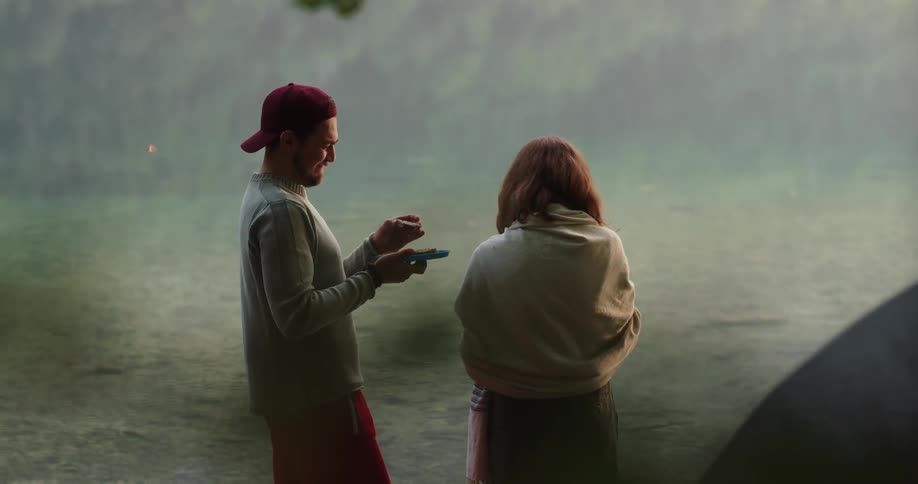 Man feeds food to woman then they smile and kiss while standing on shores of lake