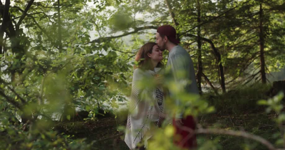 A man hads a woman a cup of coffee and kisses her before walking away as they stand in a forest during the day