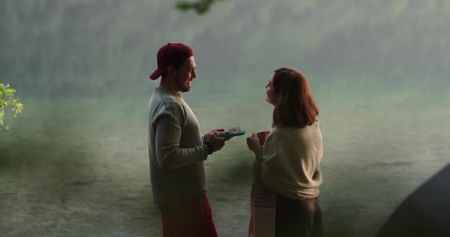 A man walks up to his girlfriend with a plate of food and brushes her hair aside as they stand by their tent
