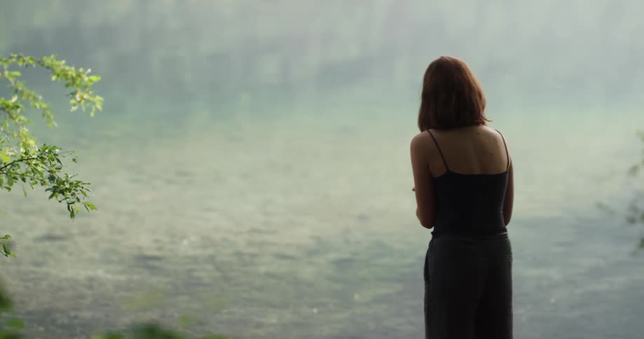 A woman is standing by a river and feeding ducks