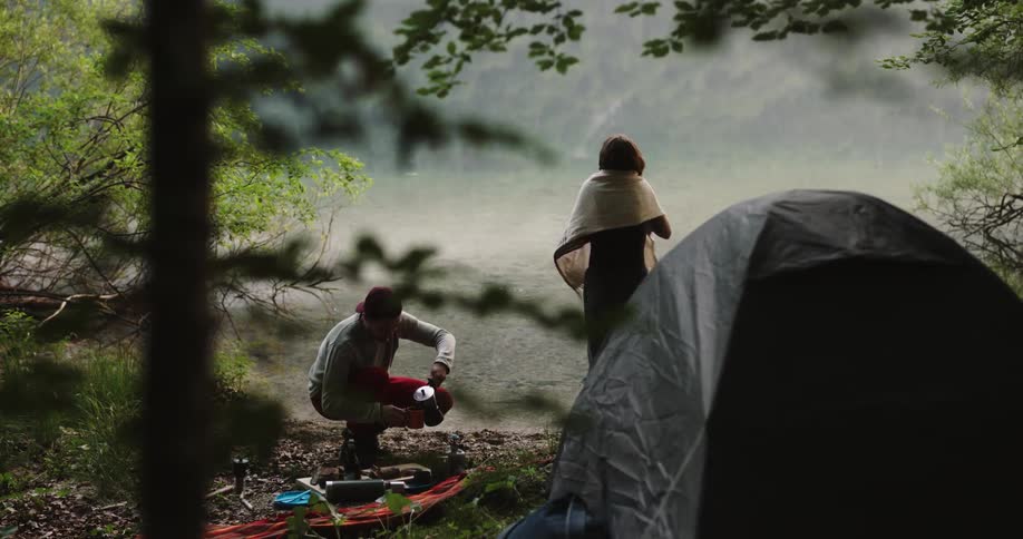 A woman exits a tent as a man pours a cup of coffee and gives it to her