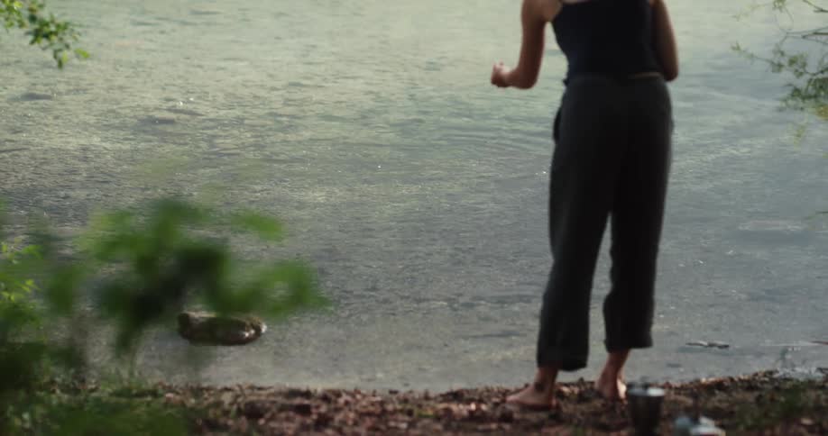 A woman stands and skips rock in a lake