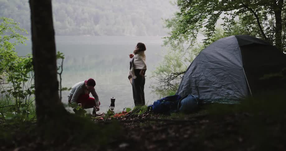 Man holds woman before the tent next to lake in the forest