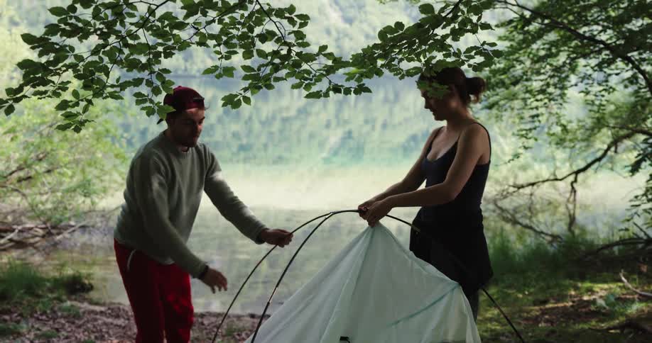 Man and woman are setting up a tent in the wilderness