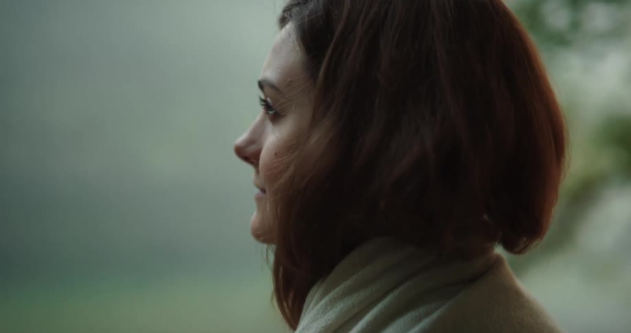 Woman with brown hair wears beige scarf and looks around in the forest