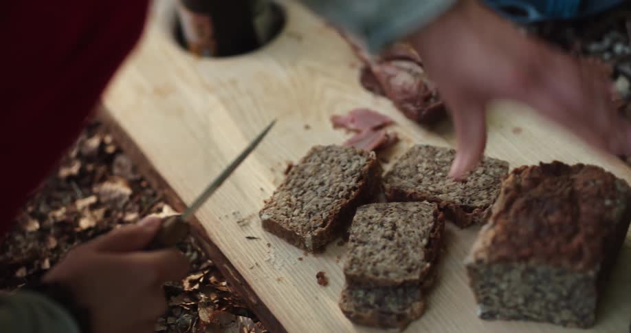 A person cutting meat and bread outdoors