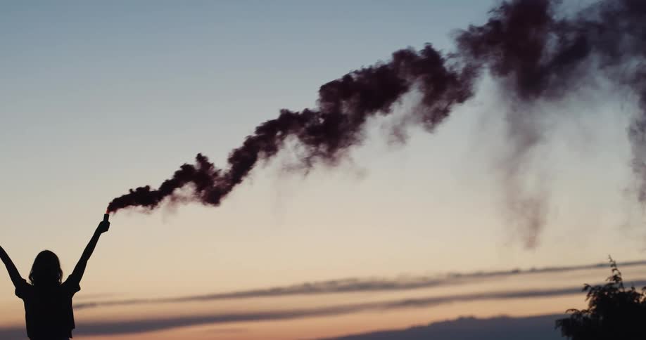 A silhouette of a woman holding a cylinder with smoke with the sky and clouds in the background