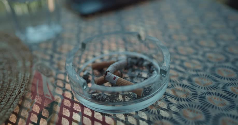 A small glass ash tray on a table is filled with a few used cigarettes