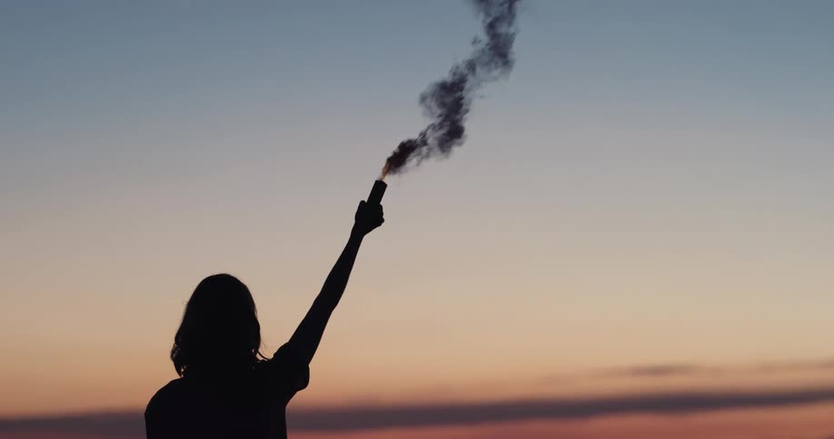 A silhouette of a woman holding up a cylinder with smoke with the sky and clouds in the background