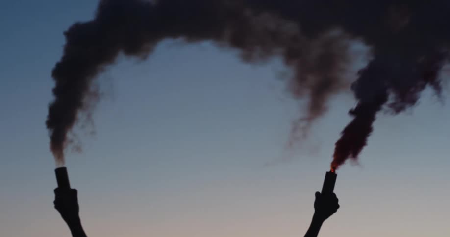A silhouette of a woman holding up cylinders with smoke with the sky and clouds in the background