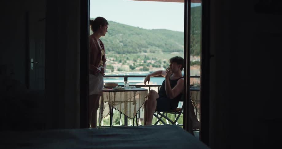 A man lights a cigarette on a balcony and a woman reaches for it