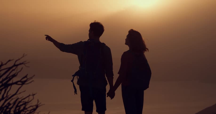 Silhouette of a young couple holding hands in front of a lake at sunset