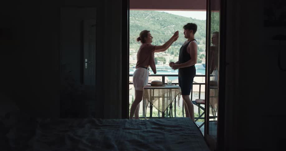 Man and woman argue on a balcony then the woman storms off and throws herself on the bed