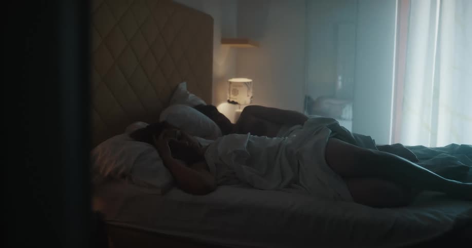 A man and woman remain asleep in bed as sunlight shines in through the window