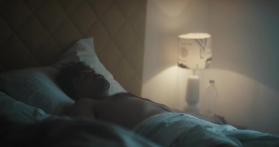 A man drinking from a water bottle while lying in bed lays back to rest for a moment before forcing himself to get out of bed
