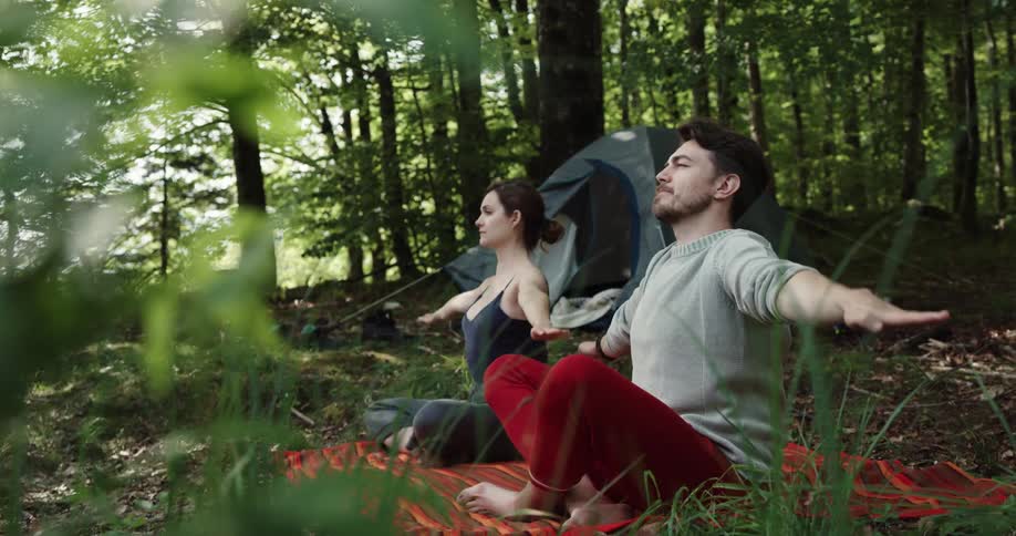 A woman and a man in a forest on a mat stretching with a tent and trees in the background