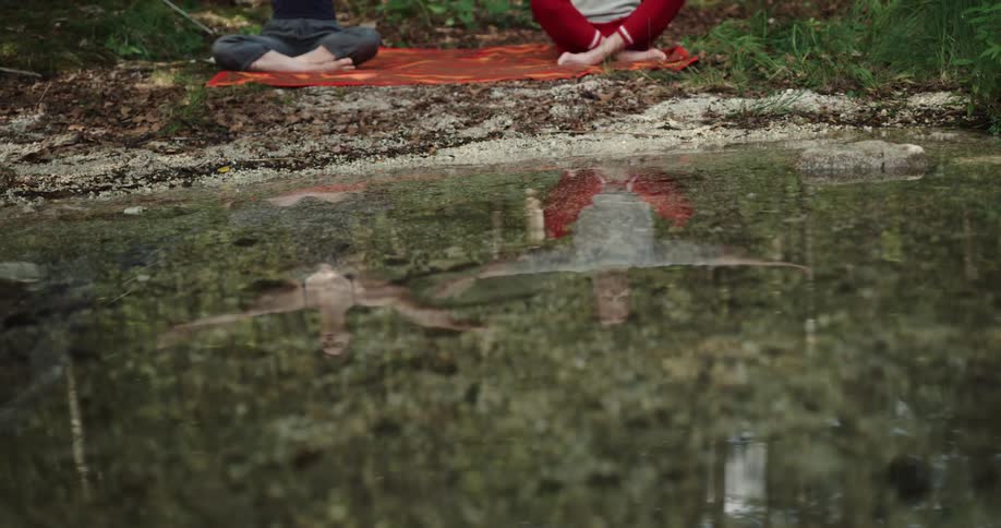 Couple sitting over a tarp on the shoreline of a lake doing yoga