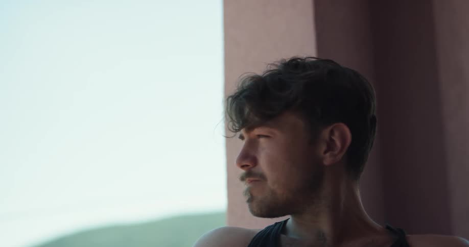 Man with a beard and a black tank top sits on the balcony