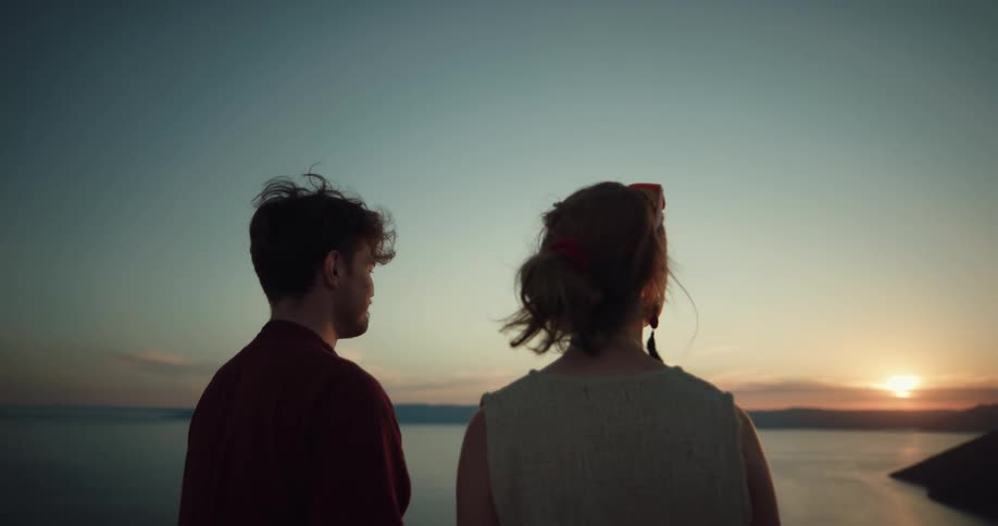 Man and woman are standing outdoors and watching the sunset