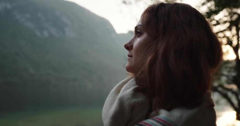 A woman wraps a blanket around herself as she stands and admires the view at sunrise