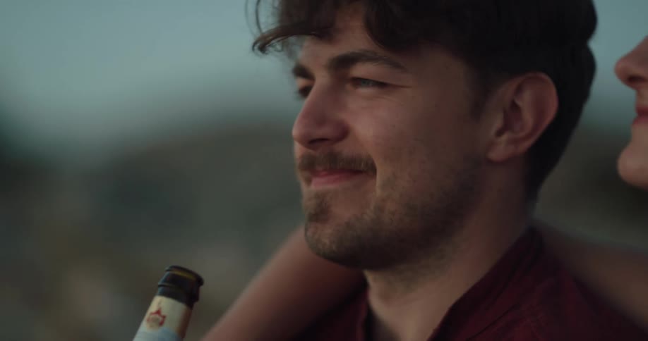 Young couple sitting outdoors hugging while playing with beer bottles