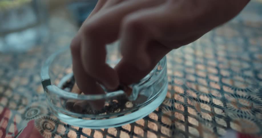 A person is sitting outdoors and putting a cigarette in an ashtray