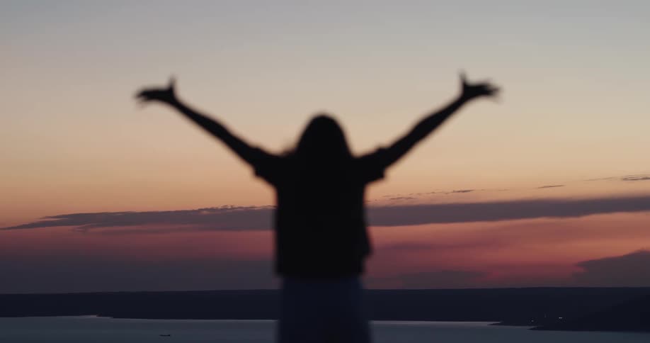 A woman is standing outdoors and looking at the sunset