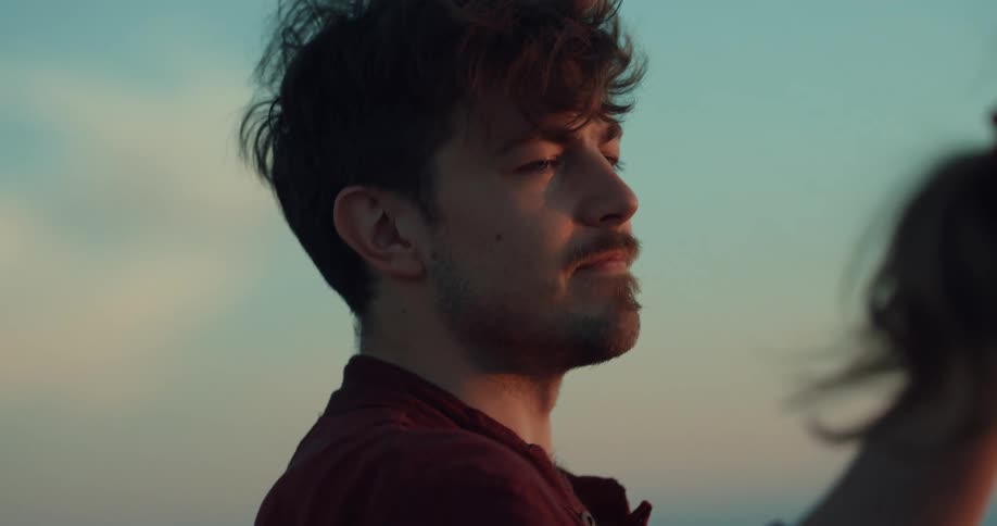 Man looks at woman caressing her head and kissing her forehead at sunset