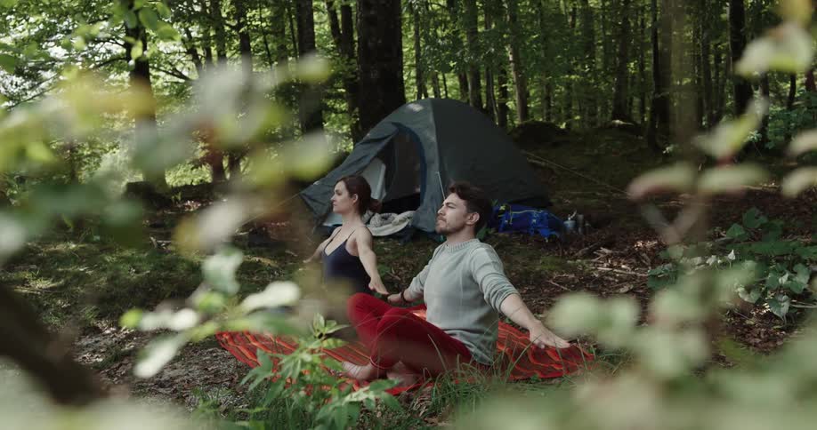 Couple does yoga next to tent in the woods