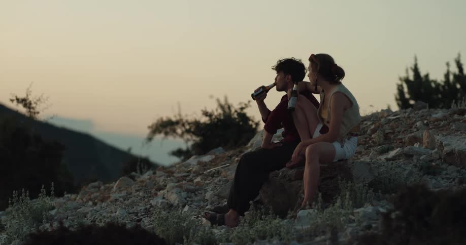 Man and woman are drinking beer outdoors at dusk