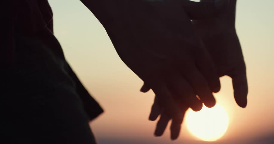 Two people are holding hands at dusk