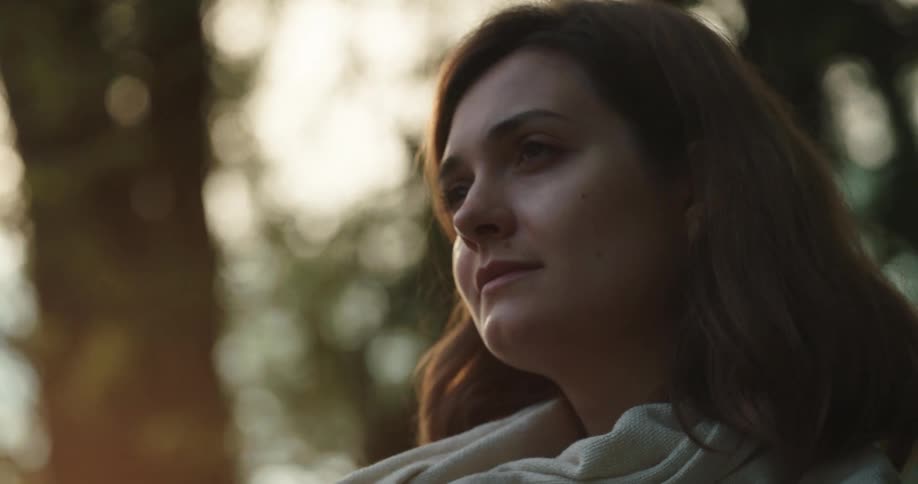 A woman is standing outdoors in a forest at dusk