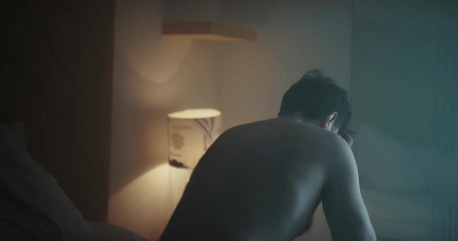 A man is sitting on a bed next to a lamp