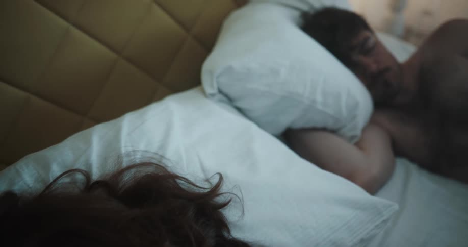 A man and a woman in a bedroom laying in a bed with pillows