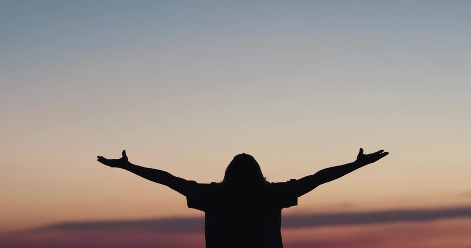 A silhouette of a woman by a lake stretching with the sky and clouds in the background