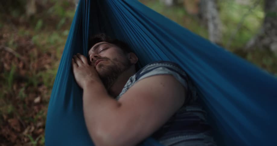 Man takes a nap over a blue hammock hanging on the forest