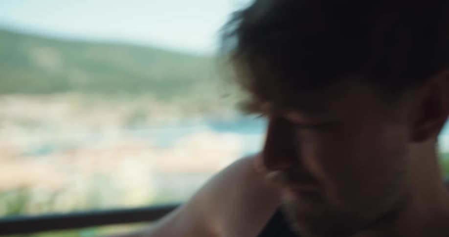 A man sitting on a balcony over the beach puts out his cigarette in disgust and takes a drink of water