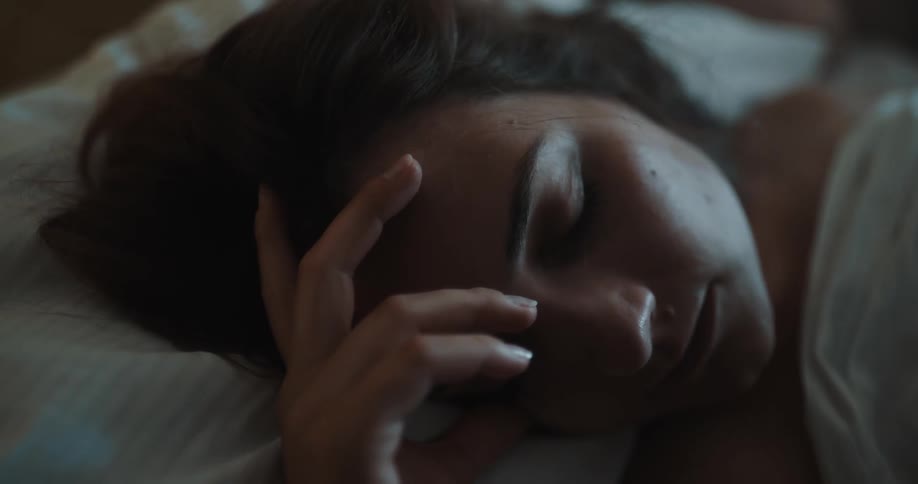 A woman asleep in bed with her hand and fingers touching her forehead