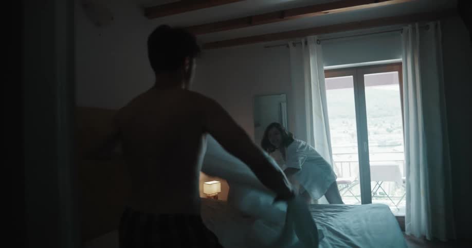 Man and woman playfully put a sheet on a bed then the woman lays down on it