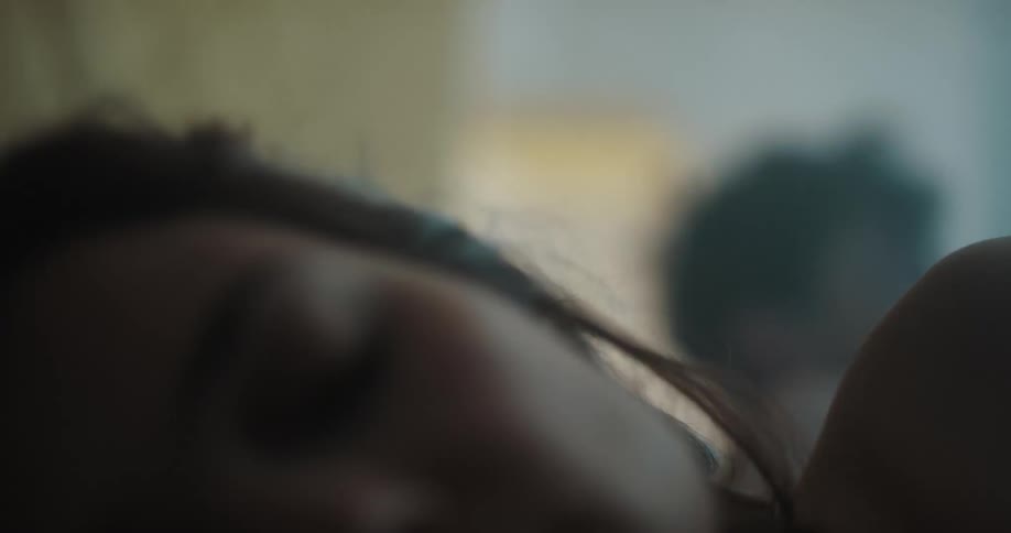 A woman in a room sleeping on a bed with a man and a wall in the background