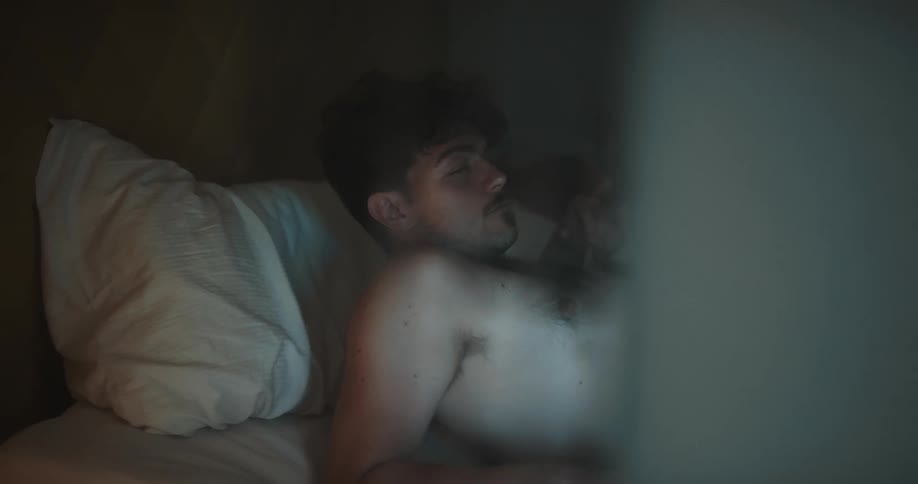 A man in a bedroom laying in a bed with a pillow with a wall in the background