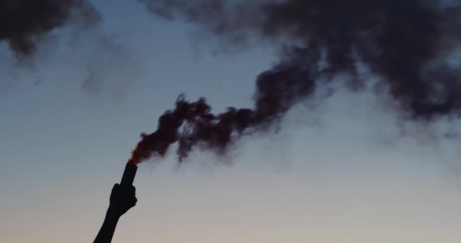 A person holds a flare up in the air and smoke billows out of it