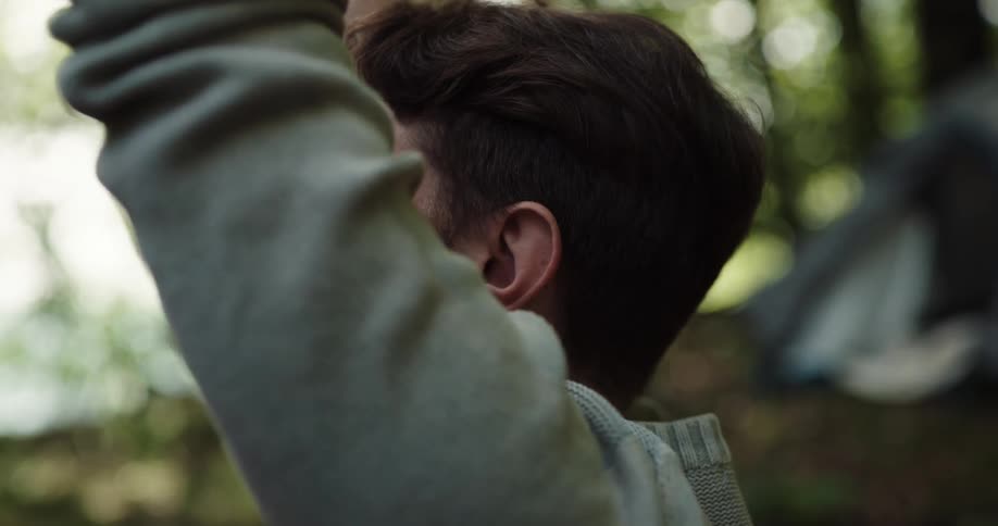 Man with a beard and a turquois sweater does yoga in the woods