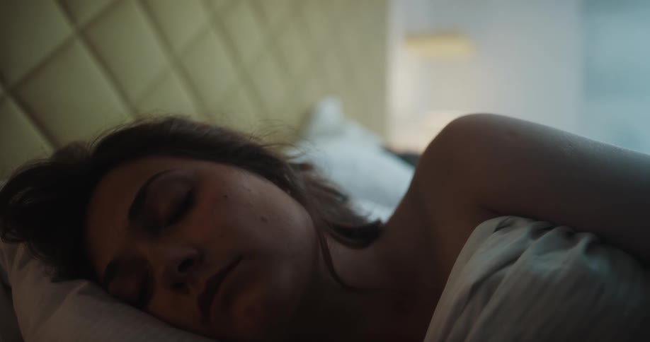 Woman lies in bed asleep under pale bedding