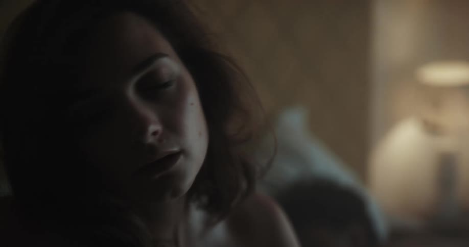 A woman is sitting up on a bed while a man lays sleeping