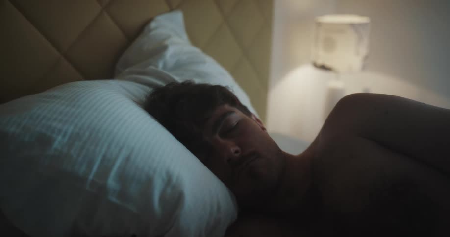 A man is sleeping on a bed with a lamp on